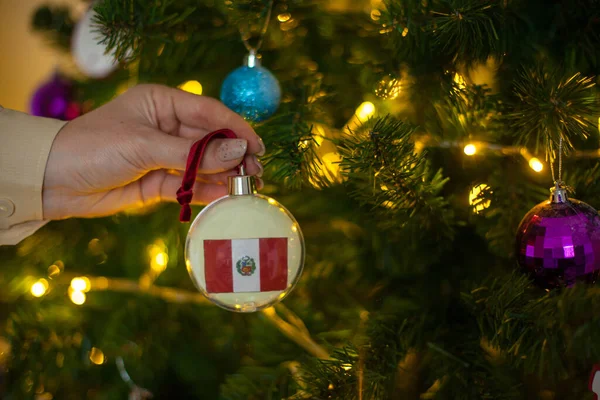 Une fille tient une décoration sur un arbre de Noël avec le drapeau du Pérou — Photo