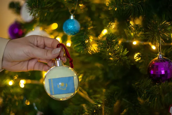 Uma menina segura uma decoração em uma árvore de Natal com a bandeira do Cazaquistão — Fotografia de Stock