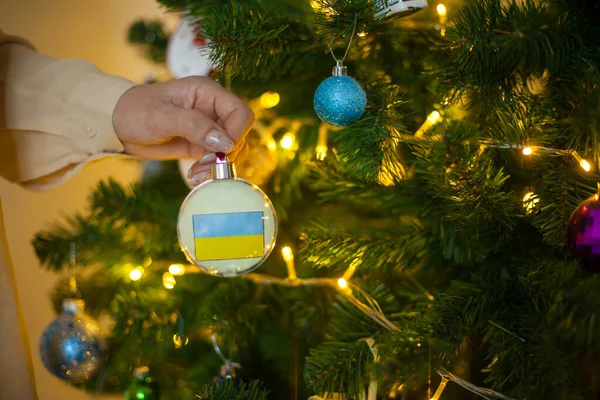 Uma menina detém uma decoração em uma árvore de Natal com a bandeira da Ucrânia — Fotografia de Stock