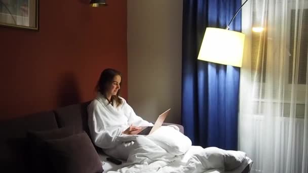 Zakelijke vrouw met een laptop in een hotelkamer gekleed in een badjas — Stockvideo