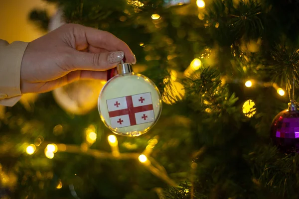 Ein Mädchen hält eine Dekoration an einem Weihnachtsbaum mit der Flagge Georgiens — Stockfoto