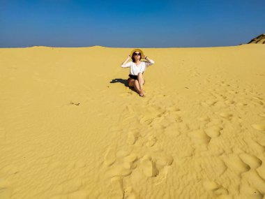 Beyaz bluzlu ve kahverengi şortlu genç bir kadın çölde yürüyor.