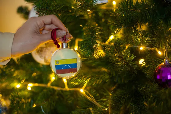 Een meisje heeft een decoratie op een kerstboom met de vlag van Venezuela — Stockfoto