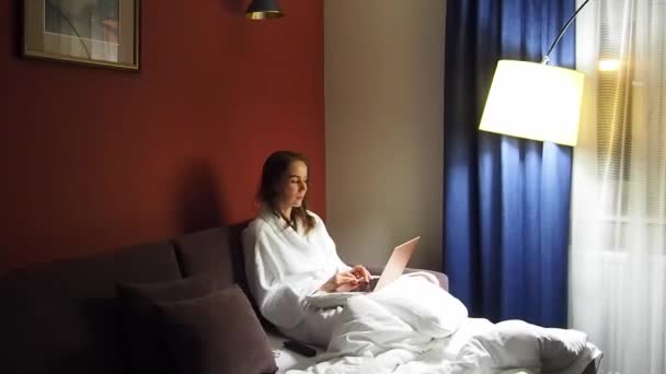 Zakelijke vrouw met een laptop in een hotelkamer gekleed in een badjas — Stockvideo