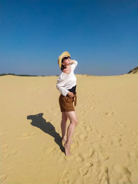Mujer joven en blusa blanca y pantalones cortos marrones caminando en el desierto — Foto de Stock