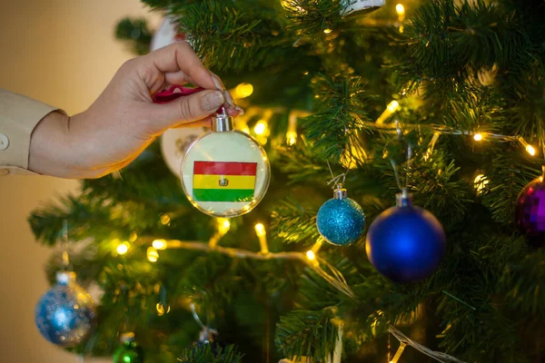 Une fille tient une décoration sur un arbre de Noël avec le drapeau de la Bolivie — Photo