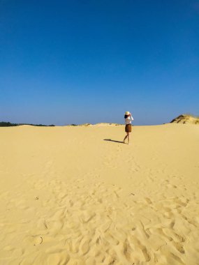 Beyaz bluzlu ve kahverengi şortlu genç bir kadın çölde yürüyor.