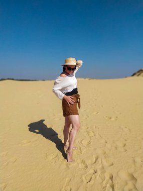 Beyaz bluzlu ve kahverengi şortlu genç bir kadın çölde yürüyor.