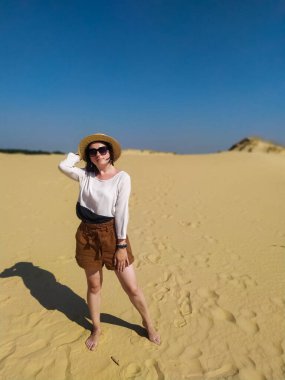 Beyaz bluzlu ve kahverengi şortlu genç bir kadın çölde yürüyor.