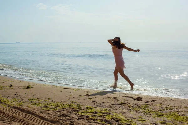Chica en vestido rosa corre en las olas del mar al mediodía. — Foto de Stock