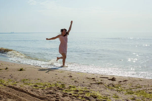 Chica en vestido rosa corre en las olas del mar al mediodía. — Foto de Stock