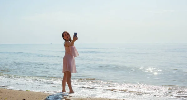 Chica en vestido rosa va en las olas del mar al mediodía. — Foto de Stock