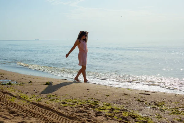 Chica en vestido rosa va en las olas del mar al mediodía. — Foto de Stock