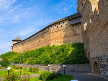 Lubarts Kalesi olarak da bilinen Lutsk Yüksek Şatosu. Ukrayna. Tuğla Kule ve Duvar. Lutsk Kalesi 'nin savunma duvarının bir parçası. Mavi gökyüzüne karşı Lords Kulesi ve tuğla bir duvarın altında yeşillik.