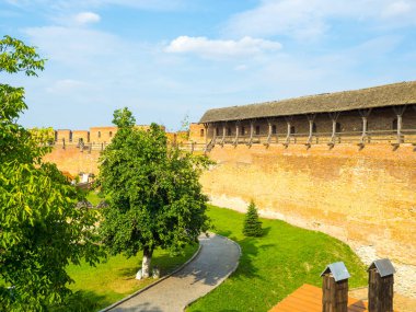 Lubarts Kalesi olarak da bilinen Lutsk Yüksek Şatosu. Ukrayna. Tuğla duvarlar ve avlu. Mavi gökyüzüne karşı Lutsk Kalesi 'nin savunma duvarının bir parçası. Yaya yolu ve yeşil ağaçları olan bir avlu.. 