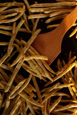 9. adım. Fırın tepsisinde pişmiş fasulye ve ahşap spatula. Kavrulmuş fasulye. Tabakta sarı ve yeşil fasulye, üst manzara. DIY. Sebze pişirme.