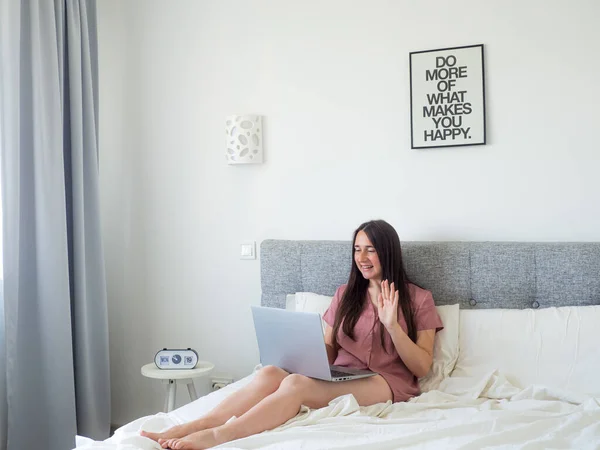 Woman working with laptop on the bed. Digital nomad and work from home concept. Young business woman working on computer, lying in the beautiful white and sunny bedroom. view with copy space