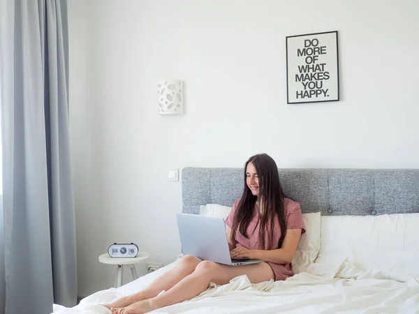 Woman working with laptop on the bed. Digital nomad and work from home concept. Young business woman working on computer, lying in the beautiful white and sunny bedroom. view with copy space