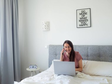Woman working with laptop on the bed. Digital nomad and work from home concept. Young business woman working on computer, lying in the beautiful white and sunny bedroom. view with copy space