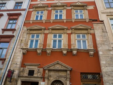 Şehrin orta kesimindeki evin kırmızı cephesi. Lviv, Ukrayna 'da saçaklarda ve sütunlarda bir aslanın kabartmaları olan dekoratif mimari. Kapının etrafında sütunlar olan bir portal. Rönesans.