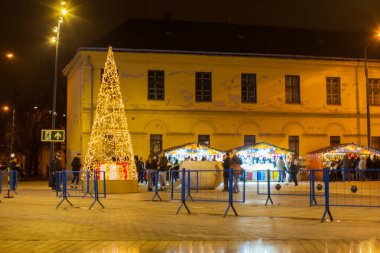 Debrecen, Macaristan - Aralık 2021: Eski Kossuth Meydanı 'ndaki tarihi Macar kenti ve geceleri yürüyen insanlar. Debrecen 'in güzel şehir merkezi ve pazar için ahşap kulübeler