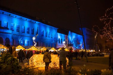 Debrecen, Macaristan - Aralık 2021: Eski Kossuth Meydanı 'ndaki tarihi Macar kenti ve geceleri yürüyen insanlar. Debrecen 'in güzel şehir merkezi ve pazar için ahşap kulübeler