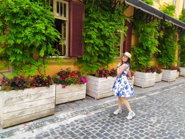 Young woman walking on the street of Lviv. Beautiful girl in white blue dress and straw hatenjoying visiting Lviv. Summer vacations.