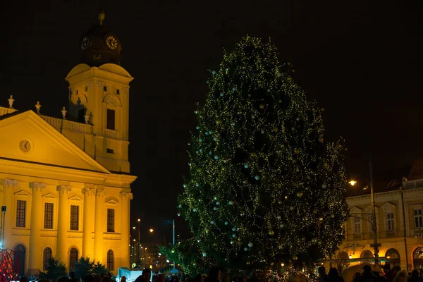 Debrecen, Hungary - December, 2021:Protestant Great Church, Hungarian: Reformatus Nagytemplom, on the Kossuth square. People near Christmas tree in front of yellow buildings at night.