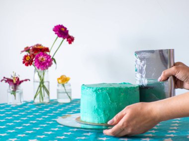 Woman spreading the icing to cover the top of the cake. Home baking, handmade. Free time on quarantine. Womens hands hold metal leveler leveling the application of cream on the cake. Selective focus.