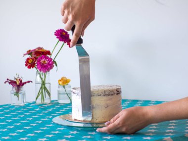 Woman spreading the icing to cover the top of the cake. Home baking, handmade. Free time on quarantine. Female hands level the cream with a spatula and cover the round cake with butter cream. DIY.