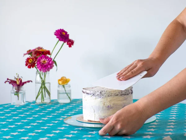 Woman spreading the icing to cover the top of the cake. Home baking, handmade. Free time on quarantine. Womens hands hold white leveler leveling the application of cream on the cake. Selective focus.