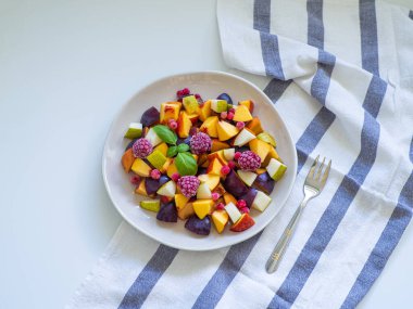 Taze erik, şeftali, nektarin, armut ve donmuş ahududu ile süslenmiş yeşil fesleğenli lezzetli meyve salatası. Üst Manzara. Sağlıklı beslenme. Uzayı kopyala Vejetaryen mutfağı. Beslenme menüsü.