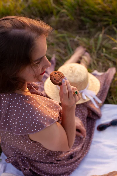 果物やペストリーと白い毛布の上に座って クッキーを食べる短い髪の長い夏のドレスの女性 夏休みや週末に街の公園でピクニックをするというコンセプト — ストック写真