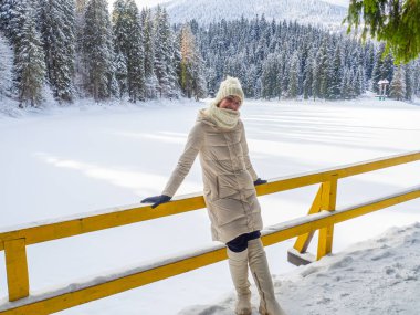 Beyaz elbiseli bir kadın Karpat dağlarında donmuş Synevyr gölünün ve ormanın tadını çıkarıyor. Kış gölü karla kaplı ormanların arasında. Parlak güneşli bir günde kozalaklı ormanlı güzel manzaralar..