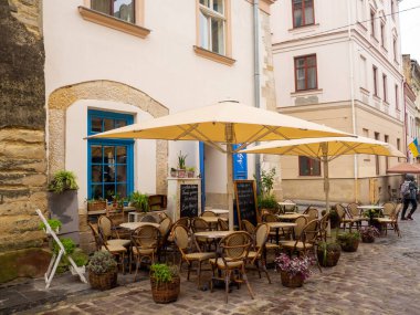 Lviv, Ukrayna - Temmuz 2022: Eski Lviv kasabasındaki rahat bir açık hava kafesi. Dar eski caddede şemsiyeli bir yazlık kafe. Asfaltlı sokakta saksıların arasında eski masalar..