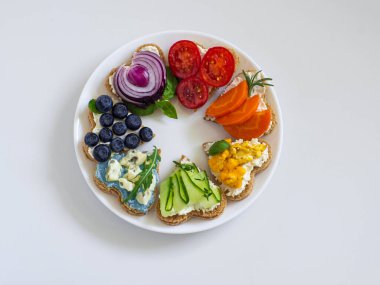 Rainbow sandwiches heart shape on white table. Breakfast bread rainbow sandwiches with colorful vegetables. Love, Valentines day food and LGBT pride flag concept. Copy space. Top view. Healthy food.