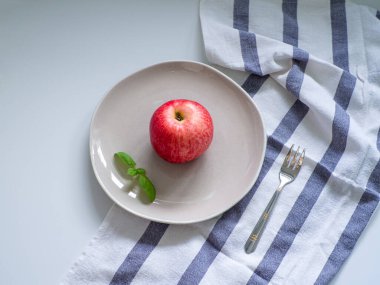 Kırmızı lezzetli elma ve yeşil fesleğen bej tabakta beyaz masa üzerinde çatal ve çizgili havlu. Diyet konsepti. Üst Manzara. Kilo verme konsepti. Uzayı kopyala, düz yat. Sağlıklı yemek ve yemek planı.