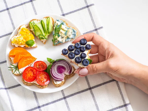 Rainbow sandwiches heart shape. Breakfast bread rainbow sandwiches with colorful vegetables. Love, Valentines day food and LGBT pride flag concept. Copy space. Hand holding blueberry sandwich.