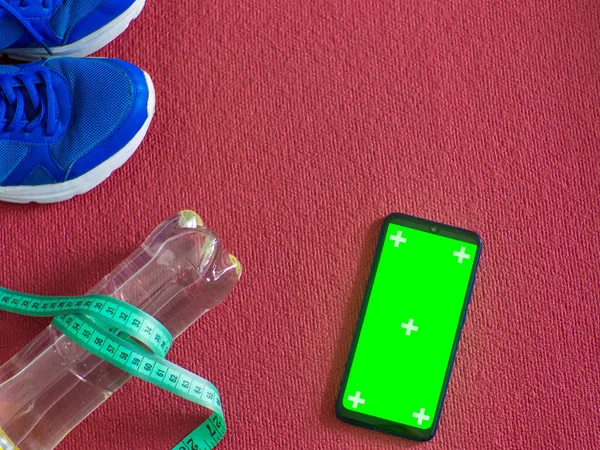 Online fitness at home. Sneakers, phone, water bottle and measuring tape on a red yoga mat background, workout online. Mockup. The concept of a healthy lifestyle, training and being fit.