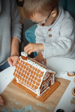 Annesiyle küçük bir çocuk Noel 'de zencefilli kurabiye evi dekore ediyor.
