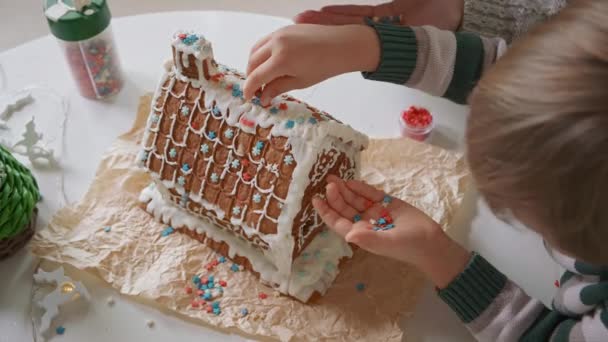 Menino com a mãe decorando casa de pão de gengibre de Natal juntos, atividades familiares e tradições no Natal e Ano Novo — Vídeo de Stock