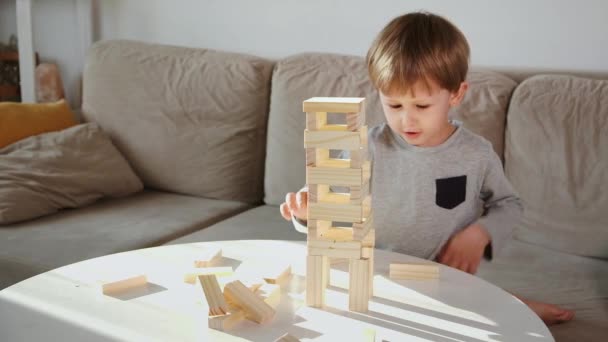 Criança bater uma torre de blocos de madeira sentado no sofá em casa — Vídeo de Stock