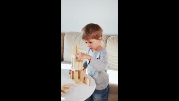 Παιδί χτίσει έναν πύργο από ξύλινα μπλοκ κάθεται στον καναπέ στο σπίτι, κάθετη βίντεο — Αρχείο Βίντεο