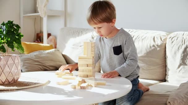 Παιδί χτίσει έναν πύργο από ξύλινα μπλοκ κάθεται στον καναπέ στο σπίτι — Αρχείο Βίντεο