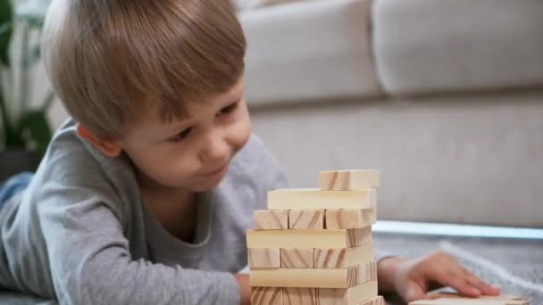 Παιδί χτίζει ένα ξύλινο πύργο για να παίζουν με ξύλινα μπλοκ που βρίσκονται στο πάτωμα στο σπίτι — Αρχείο Βίντεο