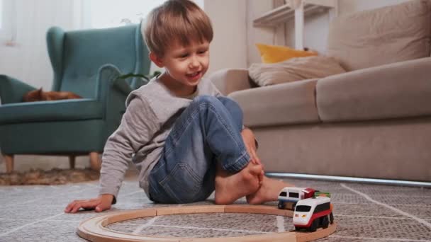 Dziecko buduje drewnianą kolej, uruchamia elektronikę parową siedząc na podłodze w domu — Wideo stockowe