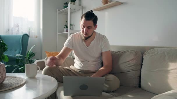 Młody Człowiek Pijący Laptopie Pijący Kawę Siedząc Kanapie Domu — Wideo stockowe