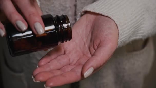 Close-up vrouw handen met witte pillen uit donkere glazen fles — Stockvideo