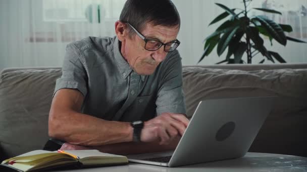 Elderly senior worried about debt payments using laptop, sitting on sofa at home — Stock Video