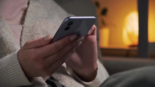 Fechar as mãos da mulher usando telefone celular em cor muito peri enquanto sentado em poltrona em casa em luz lâmpada à noite — Vídeo de Stock